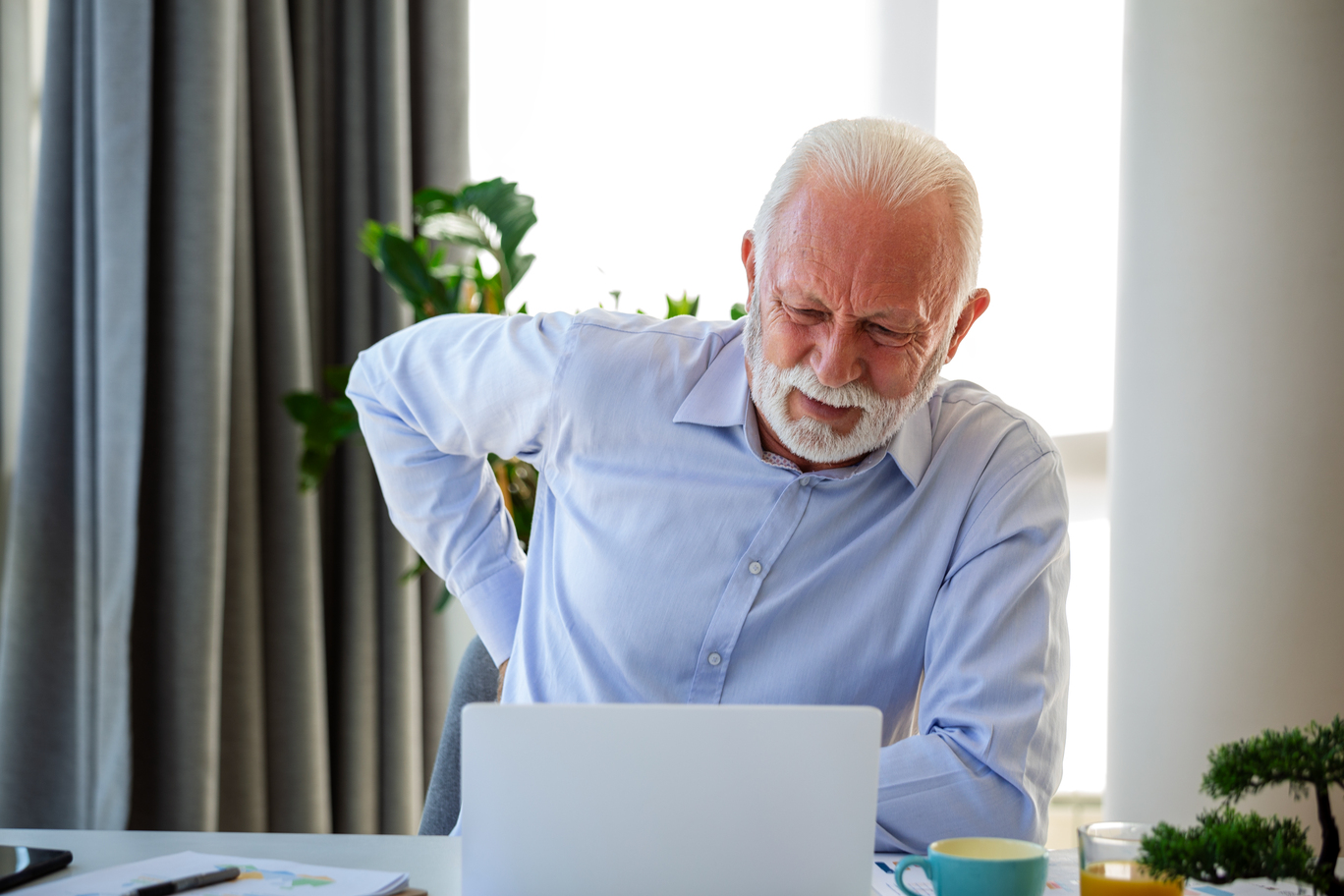 senior businessman working sitting desk suffers from lower back pain damage intervertebral discs spinal joints compression nerve roots caused by wrong posture sedentary work at Core Concept