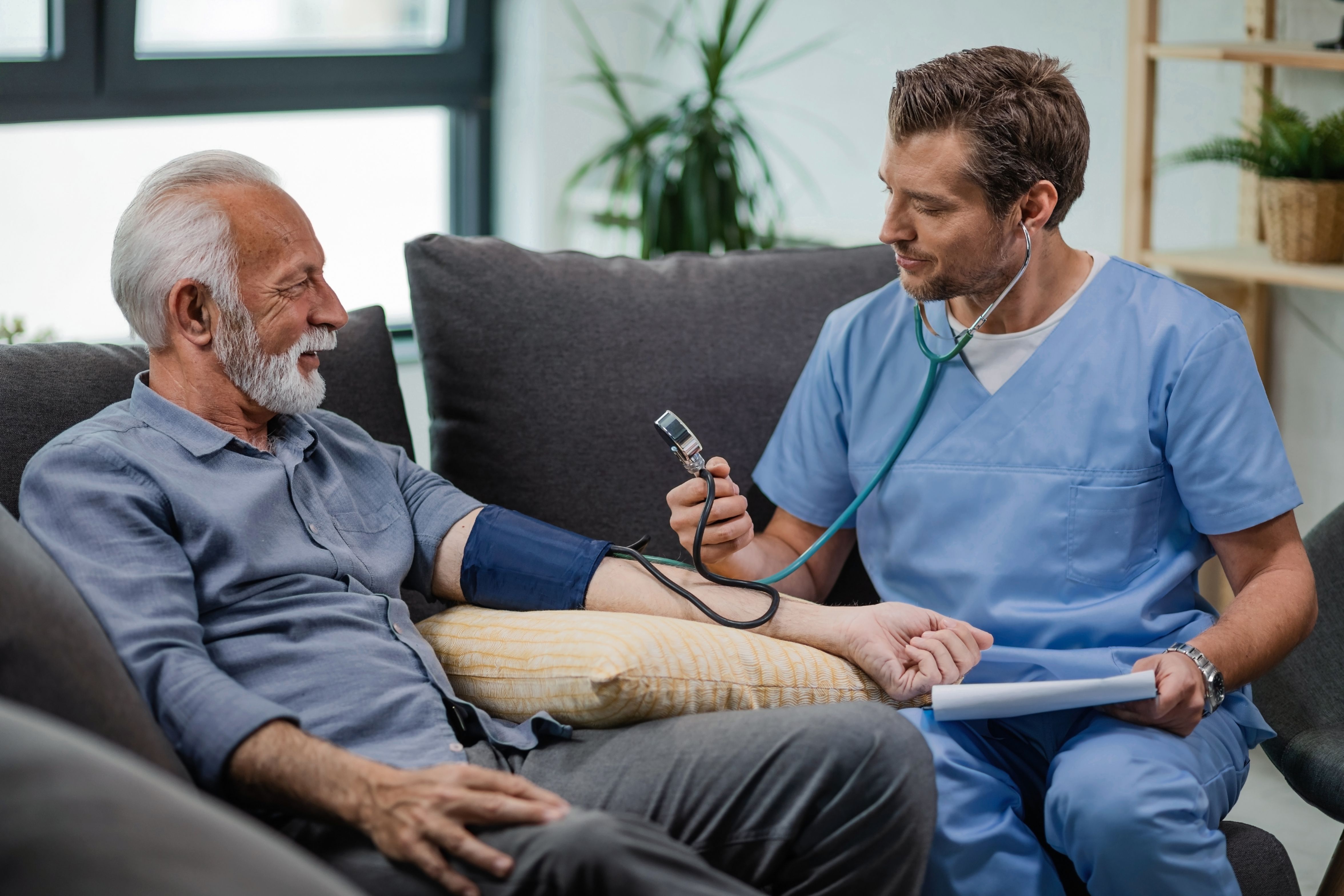 happy general practitioner measuring blood pressure mature man while being home visit at Core Concept