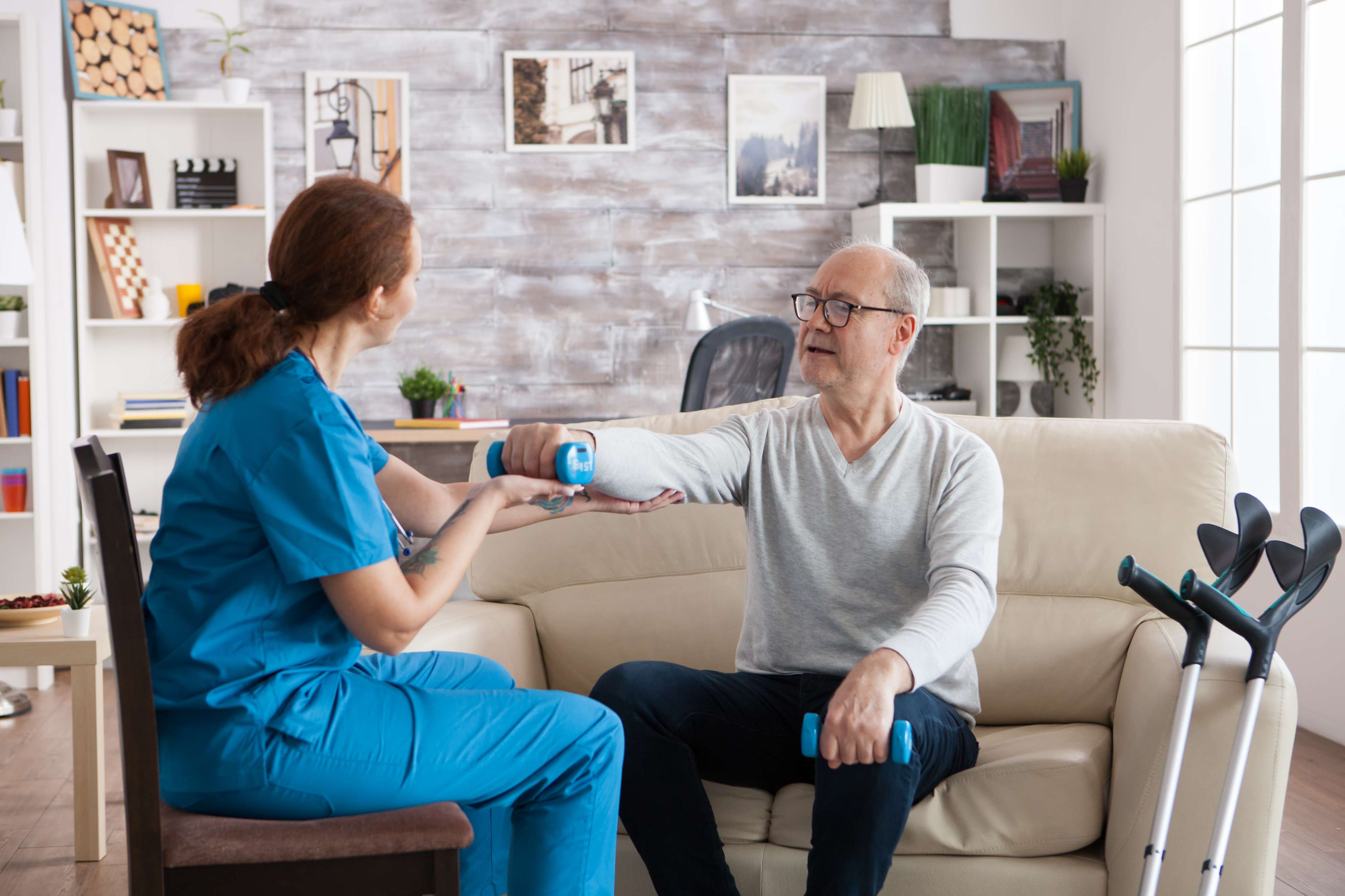young nurse doing physiotherapy treatment nursing home with senior man using dumbbells